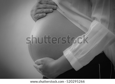 Black and white image of a pregnant woman touching her belly with hands.