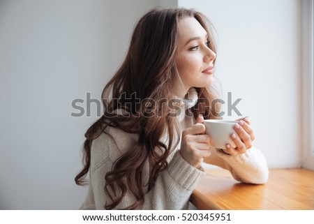 Woman in sweater with tea near the window. looking away. side view