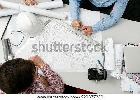 Two man analyze the diagram of a building while sitting at the table