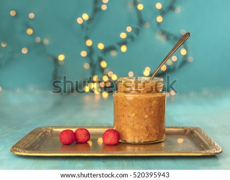 A photo of a jar of madrona (wild strawberry) fruit butter, with a spoon and madrone berries on a vintage tray, and blurred lights in the background. Selective focus