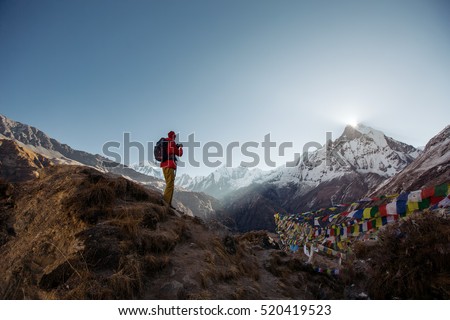 Tourist man watching and taking mobile photo of sunrise over the sacred mountain Machapuchare from Annapurna Base Camp in Himalaya Mountains