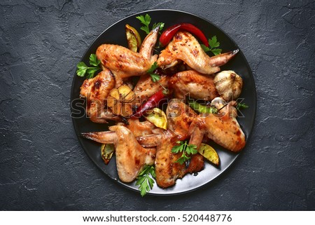 Grilled chicken wings on a black plate on a stone,concrete or slate background.Top view. Royalty-Free Stock Photo #520448776