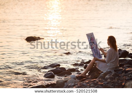 Girl artist paints a picture at sunset by the sea.