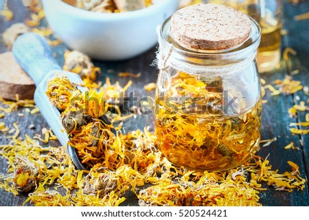 Bottles and dried calendula officinalis petals with macerated oil on wooden background. Selective focus