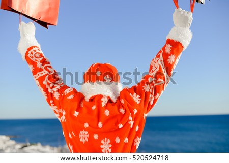 Happy Santa Claus holding shopping bag ready for joyful Christmas time on sunny blue sky outdoors background. Closeup image