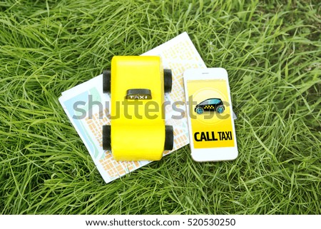 Yellow toy taxi cab, smartphone and map on green grass background. Taxi service application on phone screen.