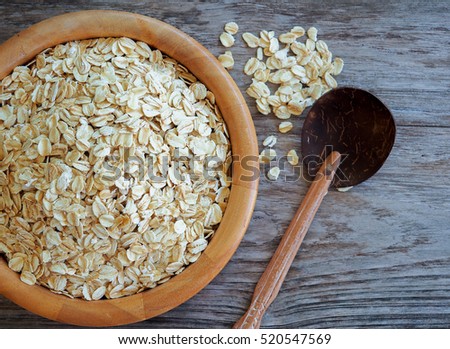 Old fashioned rolled oats in wooden bowl on wood table.