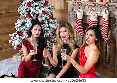 Three young woman with a glass of champagne sitting  in front of fireplace and  New Year, Christmas tree