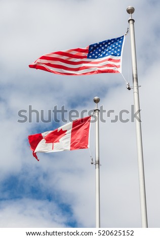 American and Canadian flag on poles hanging on a flag pole in the sky