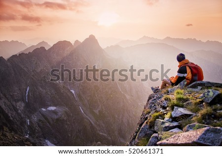 Young tourist, hiker with backpack siting on the top of the hill of mountains and looking at beautiful summer sunset Royalty-Free Stock Photo #520661371