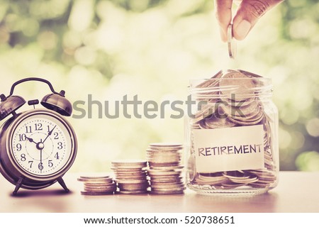 Hand putting Coins in glass jar with retro alarm clock  for time to money saving for retirement concept , vintage retro color tone Royalty-Free Stock Photo #520738651