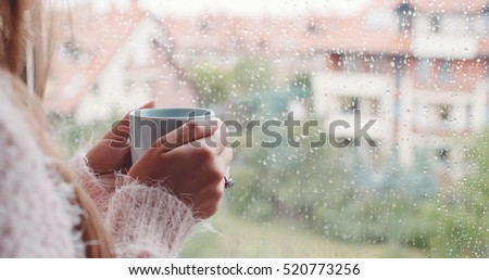 Young Woman Enjoying her morning coffee or tea, Looking Out the Rainy Window. Beautiful romantic unrecognizable girl drinking hot beverage at cozy home. Rainy Day Mood. Royalty-Free Stock Photo #520773256