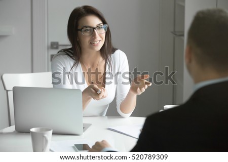 Young friendly smiling businesswoman wearing glasses talking to a male candidate at the desk, interviewing a job applicant. Rear view at a man. Business concept photo