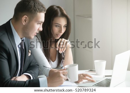 Young businessman and businesswoman sitting at the office desk, office workers looking at the laptop, discussing business ideas in collaborative form. Business concept photo