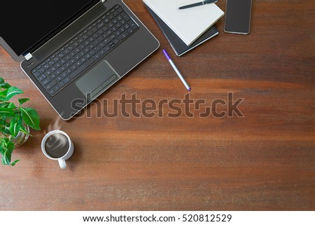 Laptop with office supplies, crumpled paper, green plant and hot black coffee with smoke on vintage grunge wooden desk background view from above, business concept