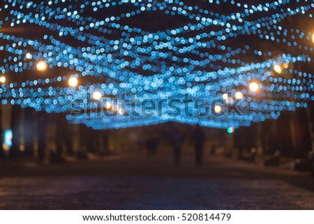 Silhouettes of people walking on christmas illuminated alley, blurred image