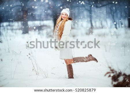 Beautiful girl with long curly hair and white clothes having fun outdoor in winter forest under snowflakes. Xmas photo.