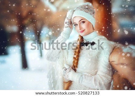 Close up winter portrait of a beautiful young girl with long braid and knitted hat standing on a background of wooden and snowflakes.