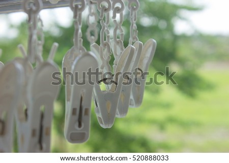 Closeup white plastic clothespin hanging on aluminum core with green nature background.