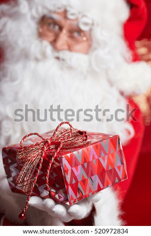 Photo of happy Santa Claus holding a gift in eyeglasses looking at camera