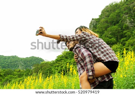 Asian handsome man is holding his girlfriend and take a photo self portrait around the field outdoor,travel in holiday on summer