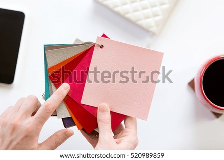 Female hands choosing a color fabric pattern above a white office desk. View from above with copy space, design concept photo. High angle view