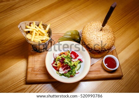 Tasty Steak Burger with Ham Slices on a Wooden Bar with fries, vegetables and Dipping Sauce.