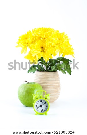 Green Apple and an alarm clock near a vase of flowers.