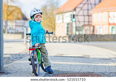 Active preschool kid boy in helmet biking on bicycle in the city. Happy child in colorful clothes and city traffic. Safety and protection for children.
