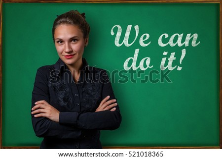 Beautiful young woman teacher (student, business woman) in classical dress standing near a blackboard with the inscription We can do it