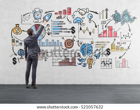 Rear view of a businessman in suit drawing a business sketch on concrete wall. Concept of business coaching