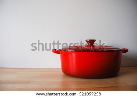 Classic Cast iron pot painted in sunburst red on wood surface with white wall background.