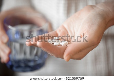 Healthcare, treatment, supplements concept photo. Woman arm holding heap of small round meds and glass of water before taking medication, shallow depth of field, focus on medicine Royalty-Free Stock Photo #521059759