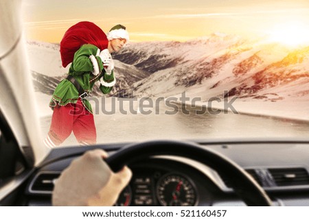 Fast driver in car interior on winter road and green young christmas elf. Photo with landscape of mountains and golden hour sunset time. 