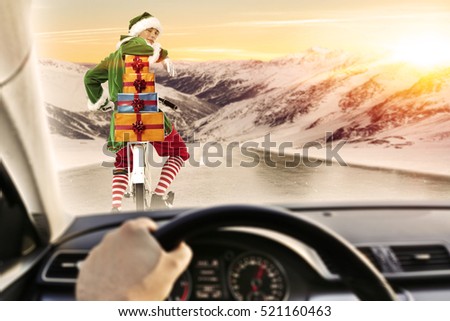 Fast driver in car interior on winter road and green young christmas elf. Photo with landscape of mountains and golden hour sunset time. 