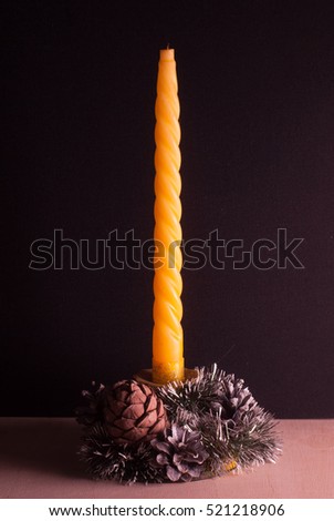 Yellow Christmas candle on black background, decorative cones, wooden table, picture for cards, happy holidays