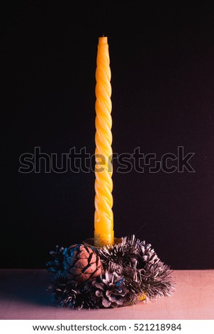 Yellow Christmas candle on black background, decorative cones, wooden table, picture for cards, happy holidays