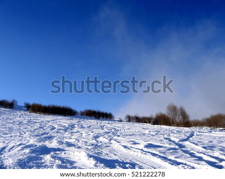 Snow covered slope on a cold and misty winter morning, with the clouds lowered to ground level