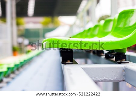 Close up chair green,green plastic stadium seats arranged in a row. The image has been made before the beginning of a tennis game,Blurred background of crowd of people at the stadium