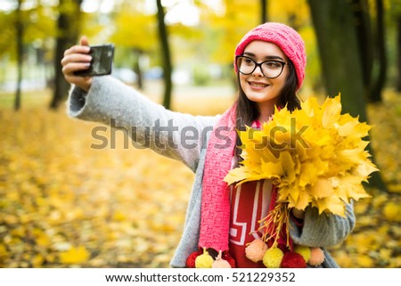 Portrait of cheerful young woman with autumn leafs in front  making selfie
