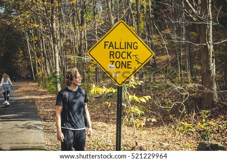 Man in black stands under the yellow sign 'Falling rock zone'