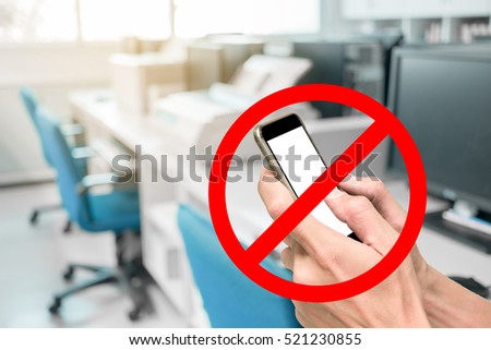 Using smartphone is not allow or prohibited in working office. Computer and desk in background. Royalty-Free Stock Photo #521230855