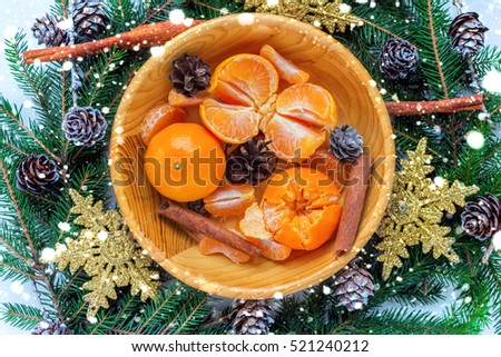 Christmas composition with tangerines, cinnamon and fir twigs in wooden plate on a festive table on a green background with snowflakes and cones fake