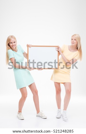 Picture of two girlfriends holding white blank desk. Isolated over white background.