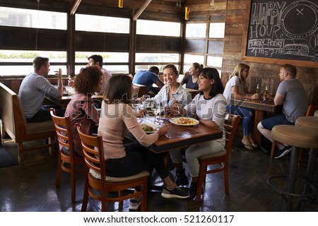 Four female friends at lunch in busy restaurant, full length Royalty-Free Stock Photo #521260117