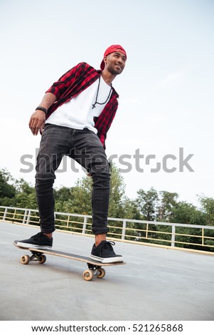 Picture of young dark skinned man wearing sunglasses and cap skateboarding. Against the nature background.