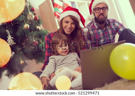 Young beautiful family sitting on the carpet on living room floor next to a nicely decorated Christmas tree and watching cartoons on a laptop computer