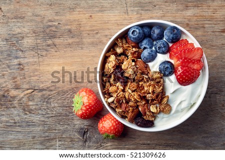 Bowl of homemade granola with yogurt and fresh berries on wooden background from top view