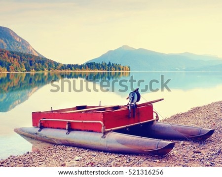 Abandoned red gray fishing boat on bank of Alpine  lake. Autumnal morning at  lake  in gentle sunlight. Picturesque scene. Mountains in water mirror.