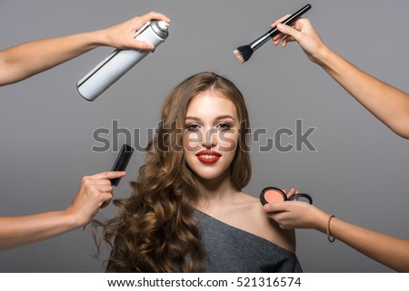 Makeup and hairstyle process, portrait of beautiful young woman and many hands with a brush, powder, comb and hairspray. Studio shot, gray background Royalty-Free Stock Photo #521316574